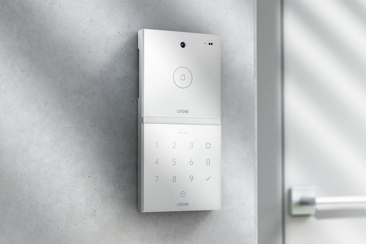 Loxone Intercom in white on a grey wall beside a door, shown with NFC Code Touch, sold separately