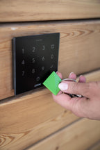 Hand holding an NFC tag to a Loxone NFC Code Touch in anthracite on a timber wall