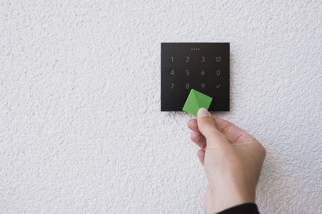 Hand holding an NFC tag to a Loxone NFC Code Touch in anthracite on a white wall