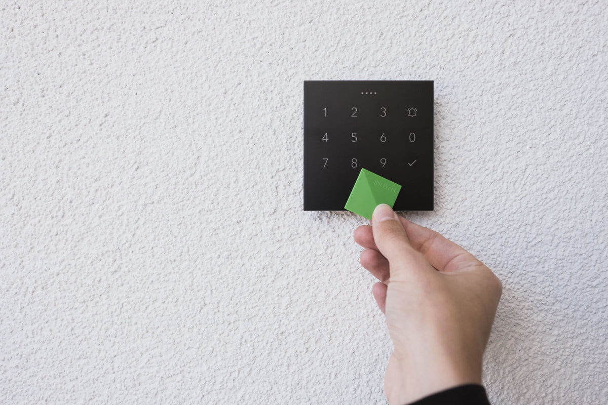 Hand holding an NFC tag to a Loxone NFC Code Touch in anthracite on a white wall